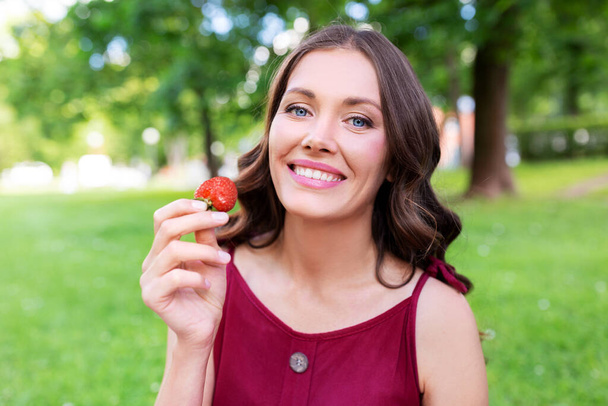 happy woman eating strawberry at summer park - Фото, изображение