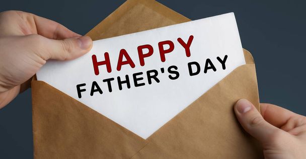 Mannelijke handen met ambachtelijke envelop met tekst HAPPY FATHER 'S DAY op blauwe achtergrond, concept - Foto, afbeelding
