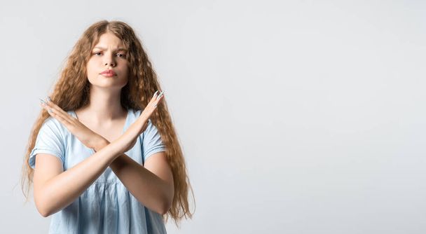 Emotional European young woman with curly long hair dressed in casual clothes, shows a STOP gesture on white background. Say NOT allow violence, STOP war make LOVE. Copy space for your text - Photo, Image