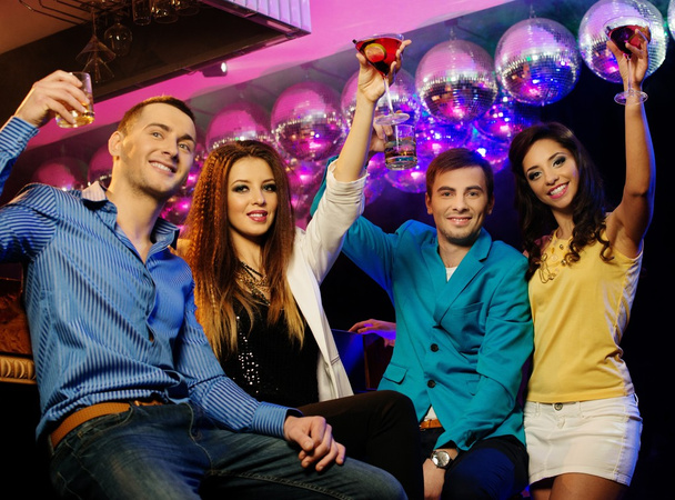 Gruppe fröhlicher junger Freunde sitzt mit Drinks im Nachtclub - Foto, Bild