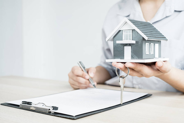 Makler, die im Bereich Immobilieninvestitionen tätig sind, halten ein Hausmodell mit Schlüsseln und Hausleasingvertrag und Hausversicherung Laut Versicherungsvertrag ist der Hauskauf für Kunden genehmigt. - Foto, Bild