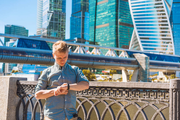 Mladý obchodník v košili se podívá na hodinky u skleněných mrakodrapů - Fotografie, Obrázek