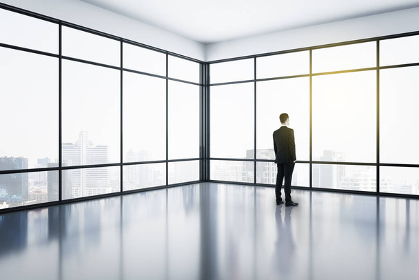 Businessman standing in modern office interior with panoramic city view. Occupation and worker concept. - Fotó, kép