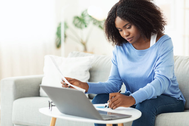 Vrouw tekent papieren die thuis op laptop werken - Foto, afbeelding