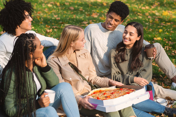 Tinédzserek csoportja, akik a földön ülve viszik el a pizzát - Fotó, kép
