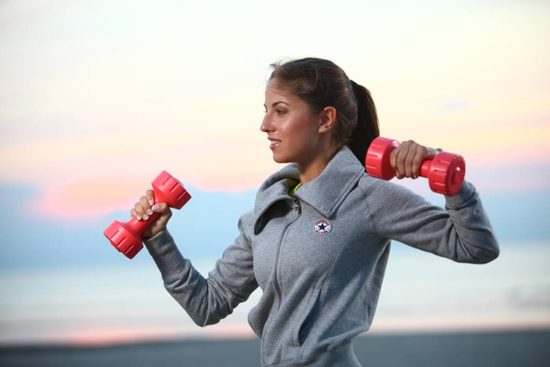 Beautiful woman doing exercises with dumbbells on the beach - Foto, immagini
