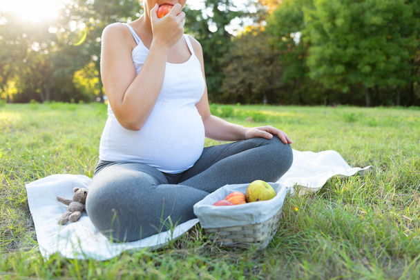 Gros plan de la jeune femme en vêtements de sport assise sur un tapis d'exercice et mangeant des pommes fraîches pendant l'entraînement à l'extérieur. S'attendre à ce que la femme fasse du yoga sur l'air frais. - Photo, image