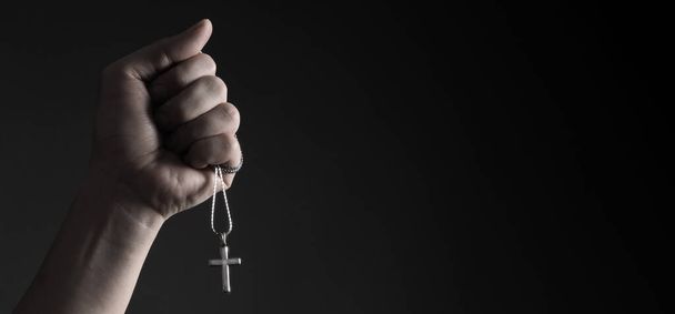 Распятие кулон или крест знак из серебра и держать в руке человека. представляют молитву за кого-то, кто уходит из мира пандемии коронавируса и крупным планом черного фона  - Фото, изображение