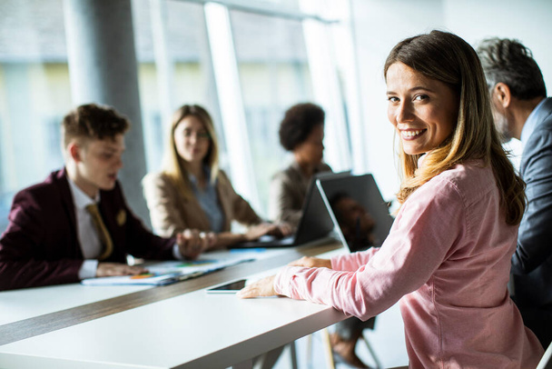 Красивая молодая женщина улыбается во время успешной деловой встречи в современном офисе - Фото, изображение