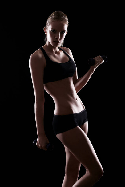 Sexy woman doing exercises with dumbells over black background - Photo, Image