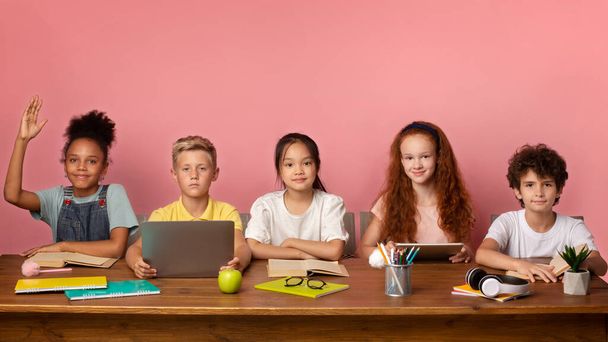 Εστιασμένη μαύρη κοπέλα και οι φίλοι της έτοιμοι να απαντήσουν στο μάθημα στο γραφείο πάνω από ροζ φόντο, ελεύθερος χώρος - Φωτογραφία, εικόνα
