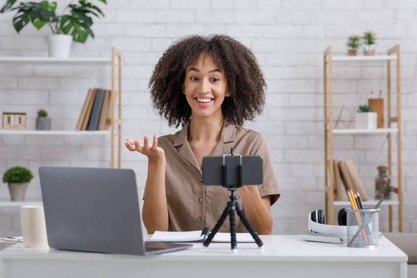 Сучасне хобі та концепція блогу. Щаслива жінка дивиться на веб-камеру, сидячи за столом в інтер'єрі
 - Фото, зображення