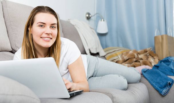 Portrait of cheerful female who is working with laptop on sofa - Foto, afbeelding