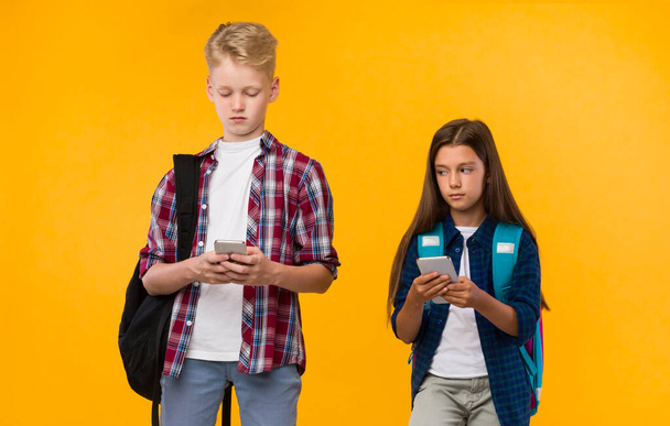 Nenucené školáci stojící s telefony na žlutém studiu - Fotografie, Obrázek