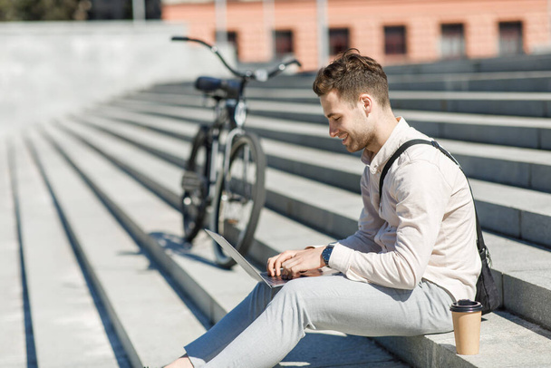 Moderne Mitarbeiter sitzen auf Treppen und vernetzen sich im Freien mit Kaffee zum Mitnehmen und Fahrrad - Foto, Bild