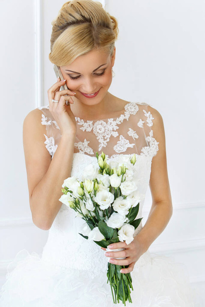 Wedding. Attractive bride with beautiful bouquet and mobile phone - Photo, Image