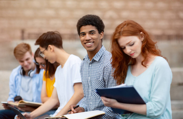 Багатокультурні студенти навчаються підготовці до випробувань сидячи за межами будівлі університету
 - Фото, зображення