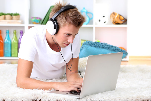 Young man relaxing on carpet with laptop - Фото, зображення
