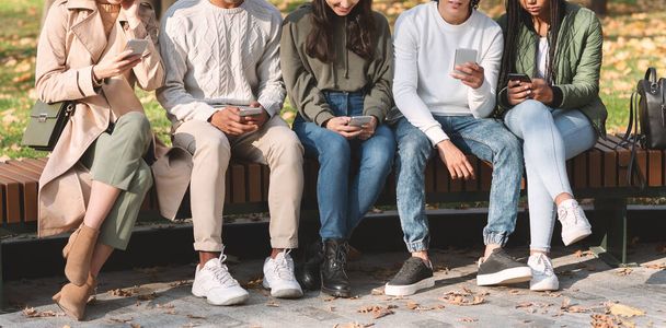 Group of international teenagers using smartphones at park - Foto, afbeelding