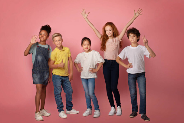 Ritratto a figura intera di scolari felici e diversi che fanno gesti diversi su sfondo rosa - Foto, immagini