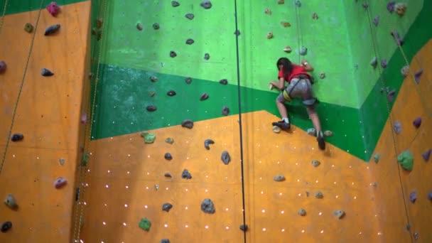 Een klein meisje klimt tegen de muur in een bouldering gym - Video