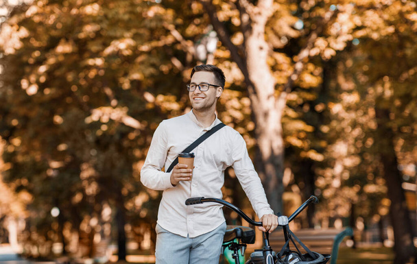 Estilo de vida moderno y transporte ecológico. Feliz hipster sosteniendo café y caminando con bicicleta - Foto, Imagen