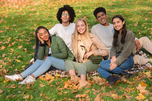 Mladí bezstarostní přátelé sedí na zemi ve veřejném parku - Fotografie, Obrázek