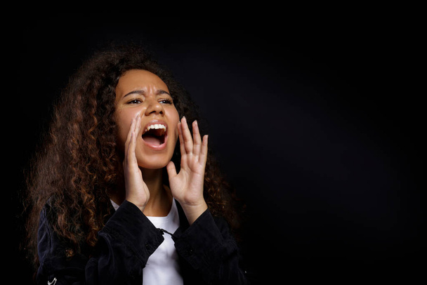 Portrait of young beautiful black woman standing in the dark showing emotions. Female with emotional facial expression over black wall background. Close up, copy space. - Foto, Bild