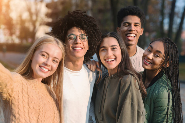 Positive multiracial teen friends taking selfie while walking in park - Valokuva, kuva