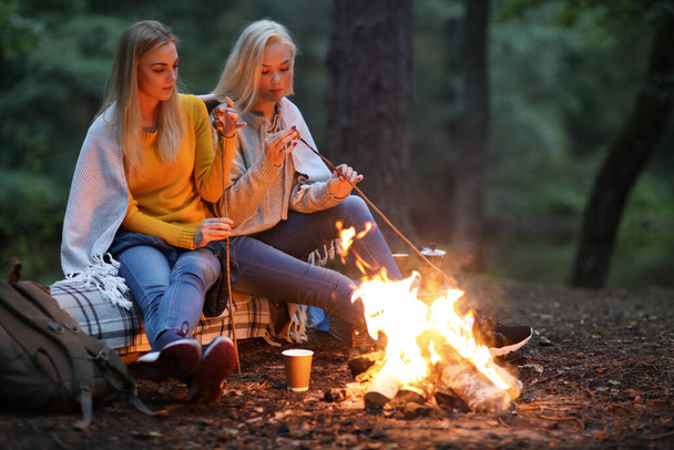 Travel and explore. Two young beautiful women near bonfire in the forest - Foto, Imagen