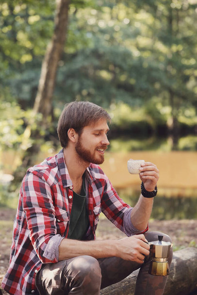 Handsome man in red plaid shirt enjoying fresh coffee in the forest - Foto, Imagem