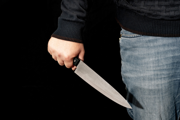 Мужская рука держит нож на черном фоне. темы насилия и убийства. вор, убийца, насильник, маньяк - Фото, изображение