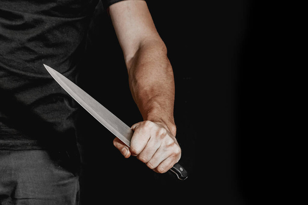 Το χέρι του ανθρώπου κρατάει μαχαίρι σε μαύρο φόντο. θέματα βίας και δολοφονίας. κλέφτης, δολοφόνος, βιαστής, μανιακός - Φωτογραφία, εικόνα