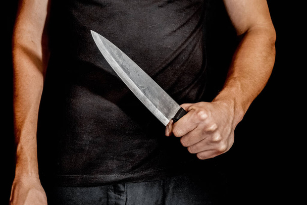 La mano del hombre sostiene un cuchillo sobre fondo negro. temas de violencia y asesinato. ladrón, asesino, violador, maníaco - Foto, imagen