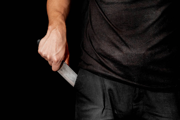 A mão do homem segura uma faca no fundo preto. tópicos de violência e assassinato. ladrão, assassino, violador, maníaco - Foto, Imagem