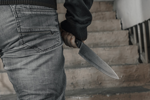 Ένας άντρας με ένα μαχαίρι στο κεφαλόσκαλο. Ο δολοφόνος κρύβεται με το μαχαίρι πριν την επίθεση. θέματα βίας και δολοφονίας. κλέφτης, βιαστής, μανιακός - Φωτογραφία, εικόνα