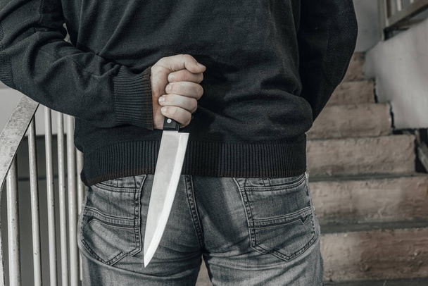 Un hombre con un cuchillo en el rellano. el asesino se esconde con cubre el cuchillo antes del ataque. temas de violencia y asesinato. ladrón, violador, maníaco - Foto, imagen
