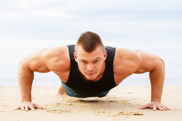 Sport, fitness. Man doet push-up op het strand - Foto, afbeelding