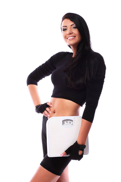 Happy fitness girl holding scales and posing over whtie background - Photo, Image