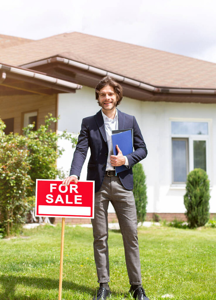 Full length portrait of property manager standing near FOR SALE sign in front of new building outdoors - Photo, Image