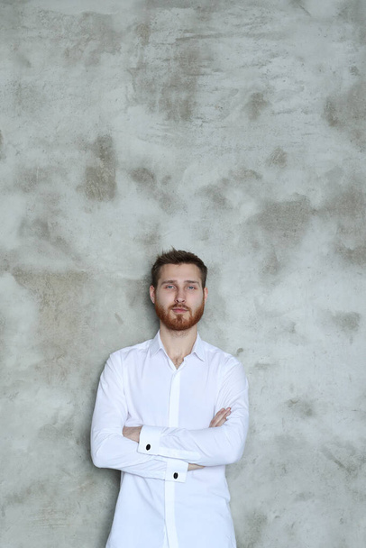 Handsome young man in a white shirt posing on grey wall - Fotografie, Obrázek