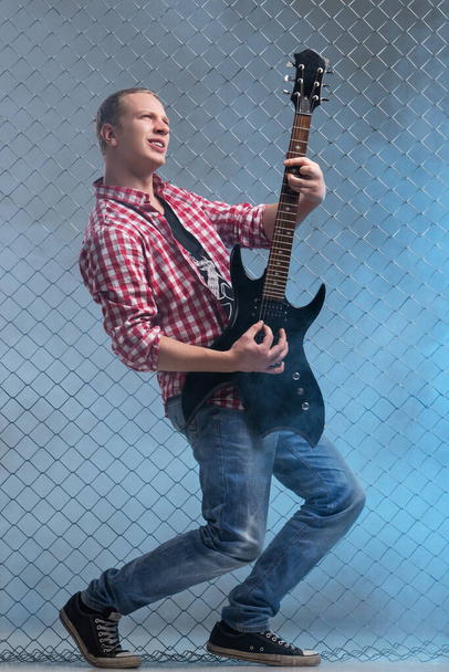 Muziek, geluid. Muzikant met een gitaar op hek achtergrond - Foto, afbeelding