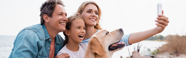 Horizontal image of family with golden retriever taking selfie on beach  - Photo, Image