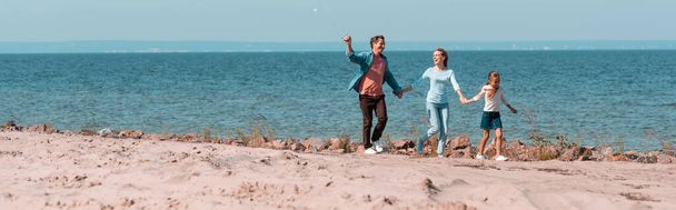 Panoramic shot of family with daughter holding hands while walking on beach  - Foto, Bild