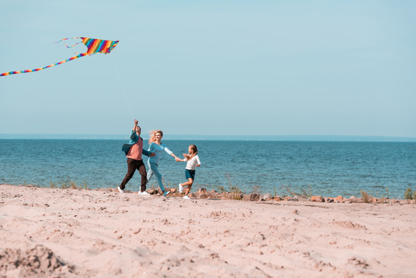 Selective focus of family with kite running on beach sand near sea  - Foto, immagini