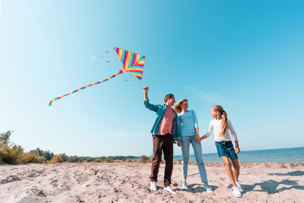 Family with child and kite holding hands on beach near sea  - Foto, Bild