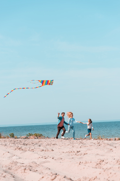 Selective focus of family with kite running on beach sand during vacation  - Photo, image