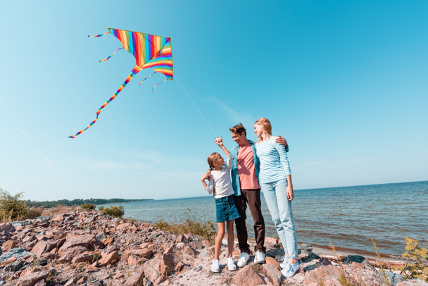 Man embracing wife and looking at daughter with kite on beach  - Valokuva, kuva