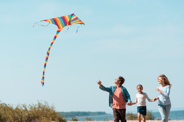 Girl running near parents with kite on beach  - Photo, Image