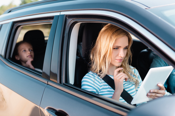 車で家族と一緒に旅行しながら、デジタルタブレットを使用して女性の選択的な焦点  - 写真・画像